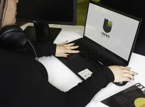 Mujer trabajando en un portátil con el logo de IBERO en la pantalla.