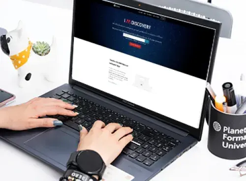 Persona frente a un portátil, al lado hay un portalápices lleno de bolígrafos.