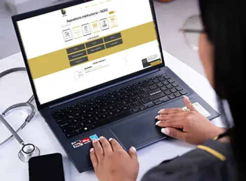 Persona frente a un portátil, con un celular y un estetoscopio al pie del equipo.