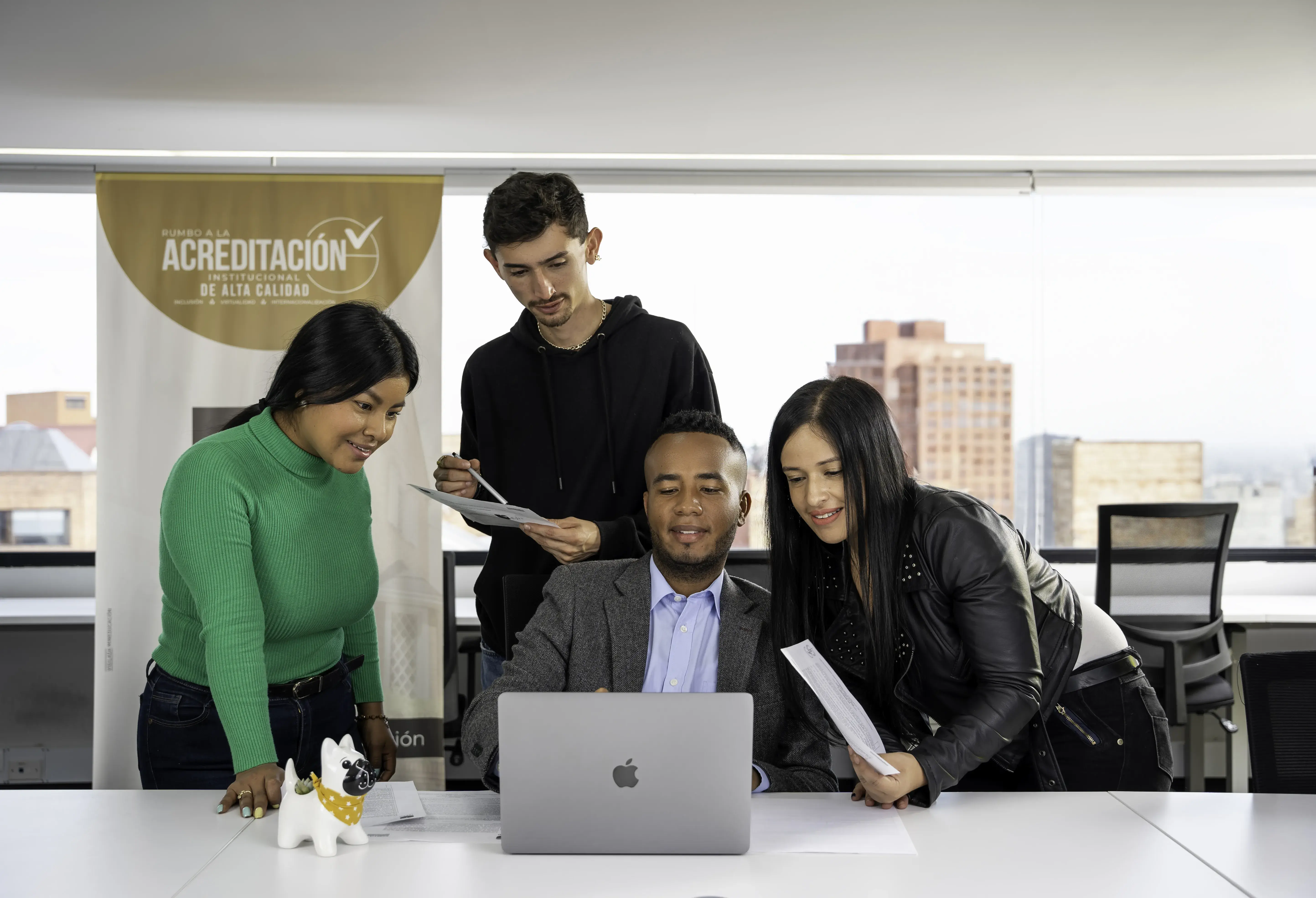 Varias personas frente a un portátil, con edificios al fondo.