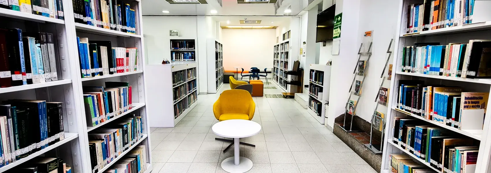 Estantes de libros a los lados y en el centro una silla y una mesa.